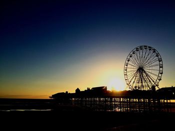 Silhouette amusement park on pier against sky during sunset