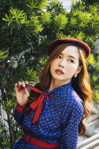 Close-up of young woman looking away while sitting on bench against plants