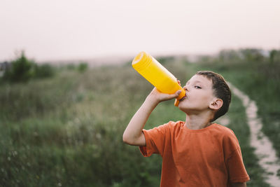 A child drinks water from a orange bottle