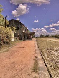 Dirt road by buildings against sky