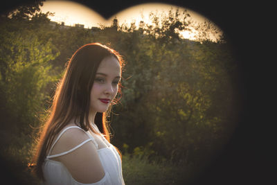 Side view of young woman standing against trees