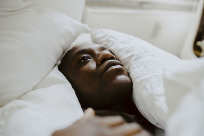 Depressed man lying amidst pillow in bedroom