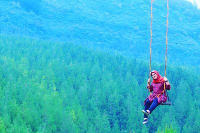 Full length of woman on swing against tree mountain