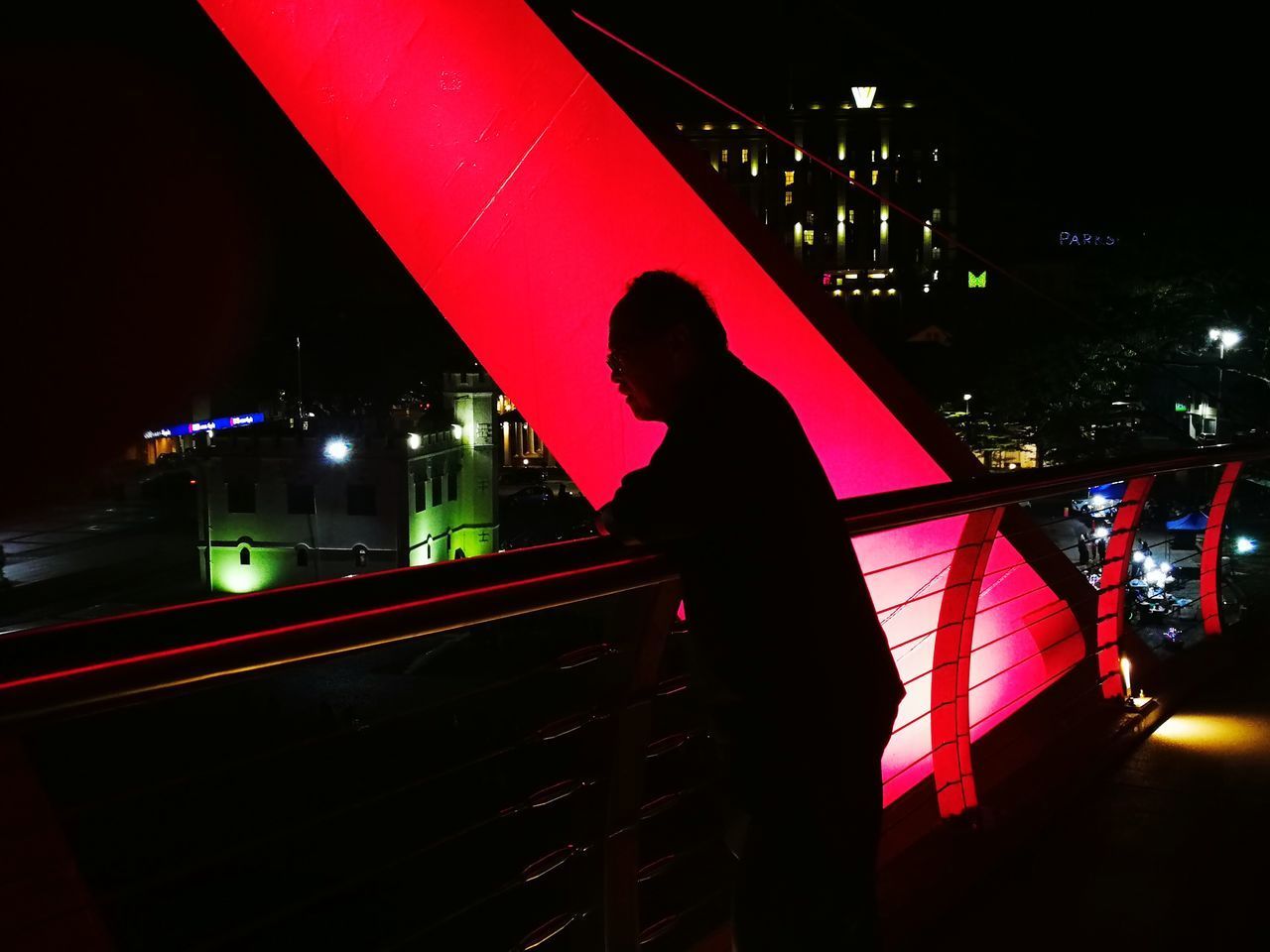 SILHOUETTE MAN STANDING BY ILLUMINATED BRIDGE AT NIGHT IN CITY
