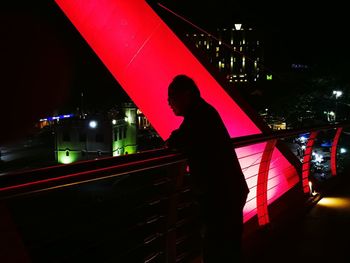 Silhouette man standing on illuminated bridge in city at night