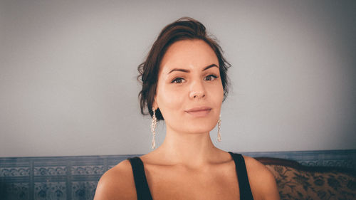 Portrait of young woman wearing earrings against wall at home