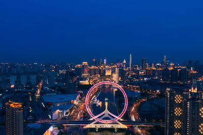 Illuminated city buildings against clear blue sky at night