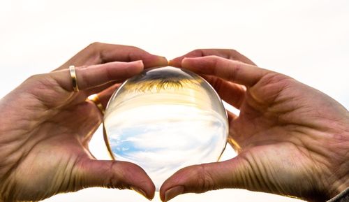 Close-up of person holding crystal ball against sky