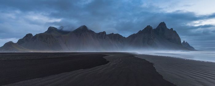 Panoramic view of mountains at beach against cloudy sky