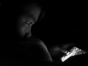 Close-up portrait of boy using mobile phone in darkroom