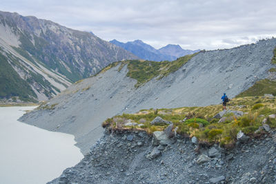 Man hiking on mountain by lake against cloudy sky