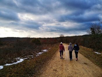 Rear view of people walking on dirt road during winter