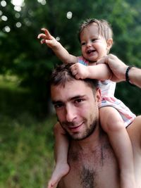 Close-up portrait of father carrying daughter on shoulder at park