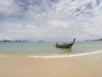 View of shore and boat at beach against cloudy sky