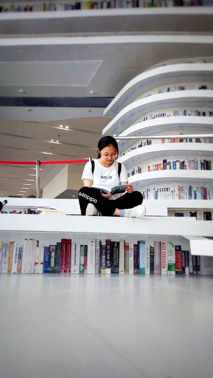 one person, real people, front view, book, architecture, indoors, publication, full length, education, sitting, concentration, young adult, portrait, learning, shelf, reading, bookshelf, men