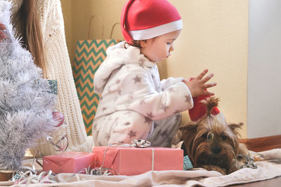 Full length of cute girl playing with christmas decoration while sitting on bed at home