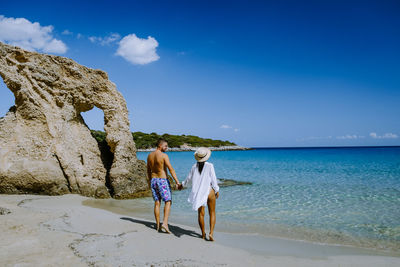 Rear view of friends enjoying at beach against sky