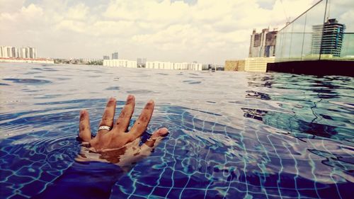 Hand by swimming pool in city against sky