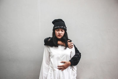 Portrait of young woman standing against white wall