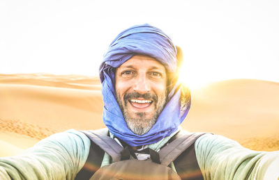 Portrait of smiling man wearing scarf at desert against sky