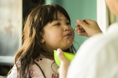 Midsection of woman feeding daughter at home