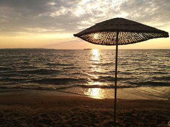 Parasol on shore at beach against sky during sunset