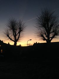 Bare trees against sky at sunset