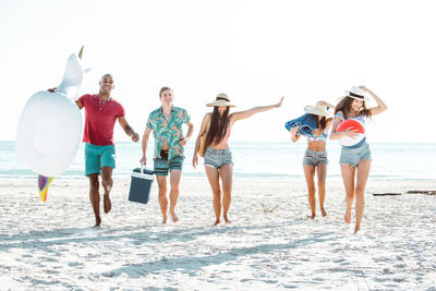 Happy friends walking on shore of beach against sky