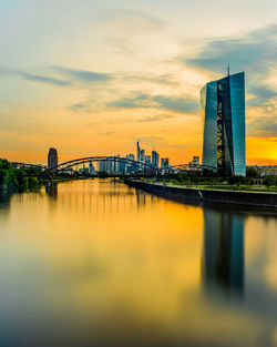 Bridge over river by buildings against sky during sunset in frankfurt, germany 