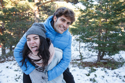 Portrait of smiling young woman giving piggyback to boyfriend on field during winter