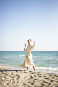 Full length of young woman standing at beach against clear sky