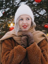 Portrait of young  stylish european woman with blonde hair near christmas tree in snowy winter day.