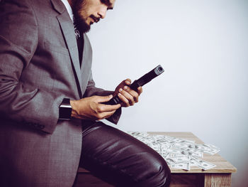 Midsection of businessman holding gun while sitting by paper currency on table