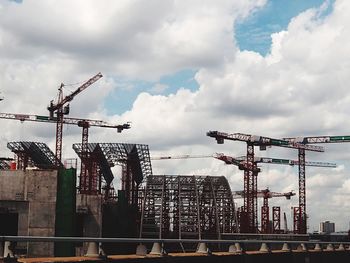 Low angle view of cranes against sky in city