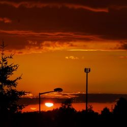 Silhouette street lights against orange sky during sunset