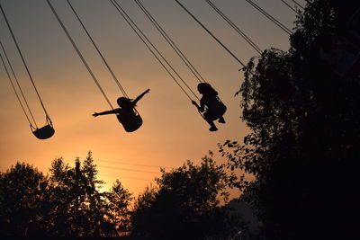 Low angle view of silhouette people in chain swing ride against sky at sunset