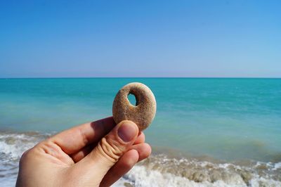 Cropped image of hand holding pebble in sea