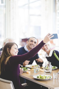 Young woman taking selfie with father and grandparents while having lunch in nursing home