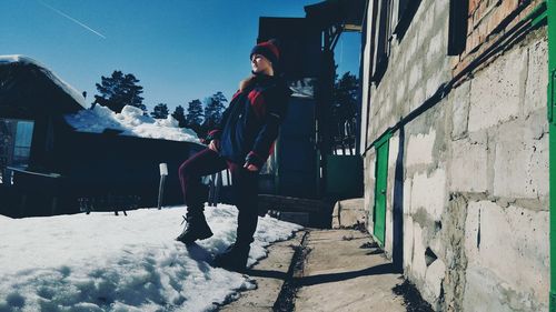 Young woman standing on snow covered field by houses