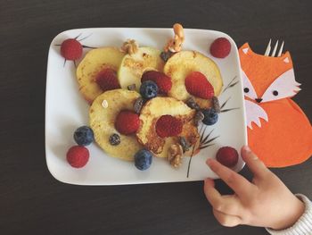 Cropped hand of child having fruit on table