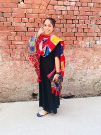 Portrait of smiling young woman standing against brick wall