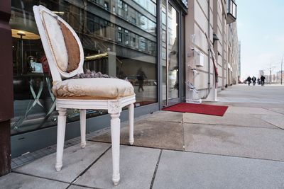Empty chairs on sidewalk by building in city