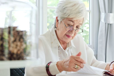 Senior woman reading book while sitting at home