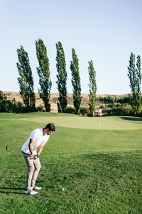 Professional male golf player preparing to hit ball with putter in green field while looking down on summer day