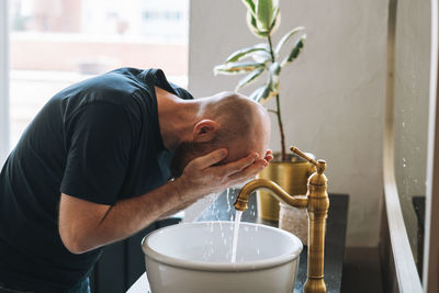 Young man washes his hands and face in sink in bathroom at home