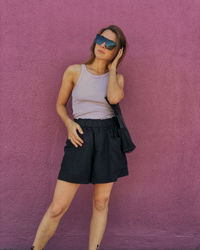 Beautiful young woman standing against pink wall