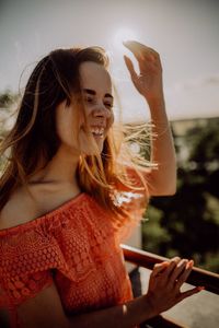 Smiling woman standing by railing against sky during sunny day