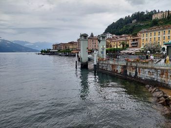 Bridge over river by buildings in town against sky