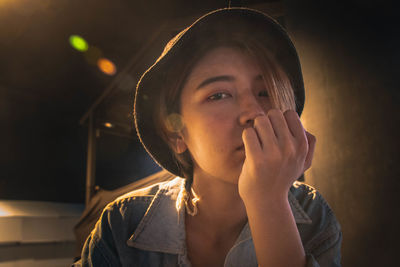 Portrait of young woman with hand on chin sitting in city at night