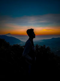 Side view of man standing on mountain against sky during sunset